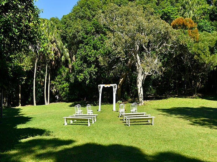 A wedding arch, benches and chairs set up on Palm Valley lawn in Cape Byron State Conservation Area.