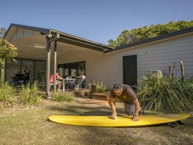 A man cleaning his surfboard on the grass nearby by the outdoor dining area at Plomer Beach House,