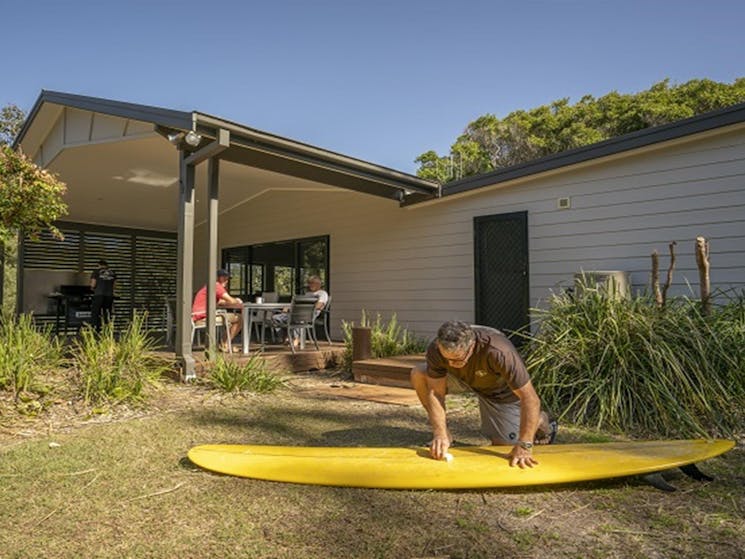 A man cleaning his surfboard on the grass nearby by the outdoor dining area at Plomer Beach House,