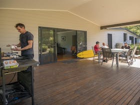 People in the outdoor dining area cooking breakfast on the barbecue and chatting at Plomer Beach
