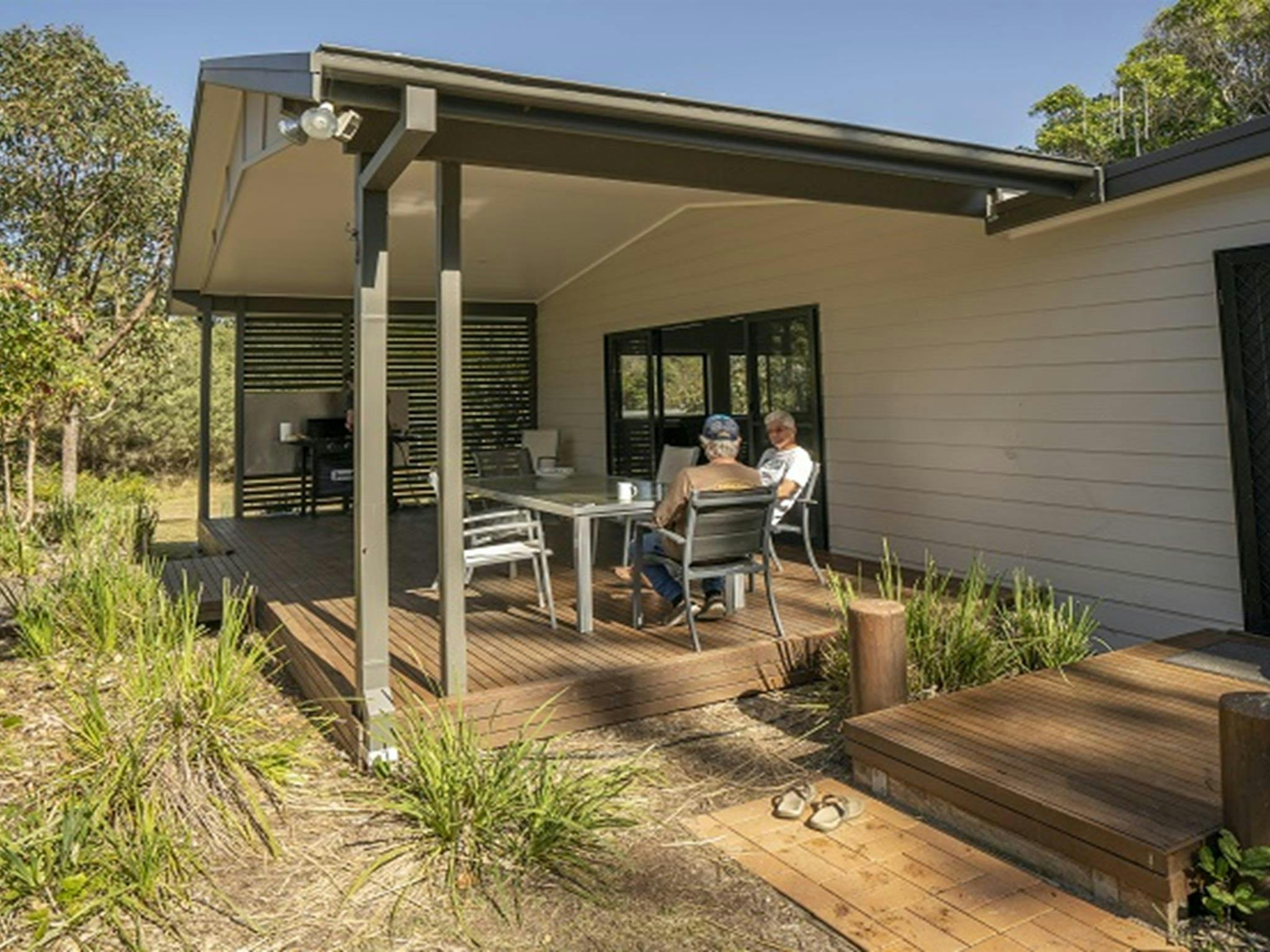 两人坐在莱姆伯纳斯普洛默海滩别墅户外用餐区的餐桌旁。