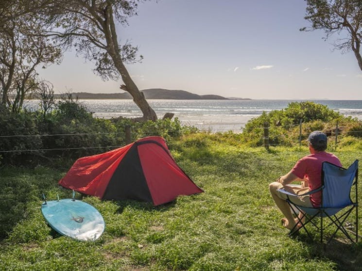 Man sitting beside his tent looking out at the ocean, at Limeburners Creek National Park. Photo: