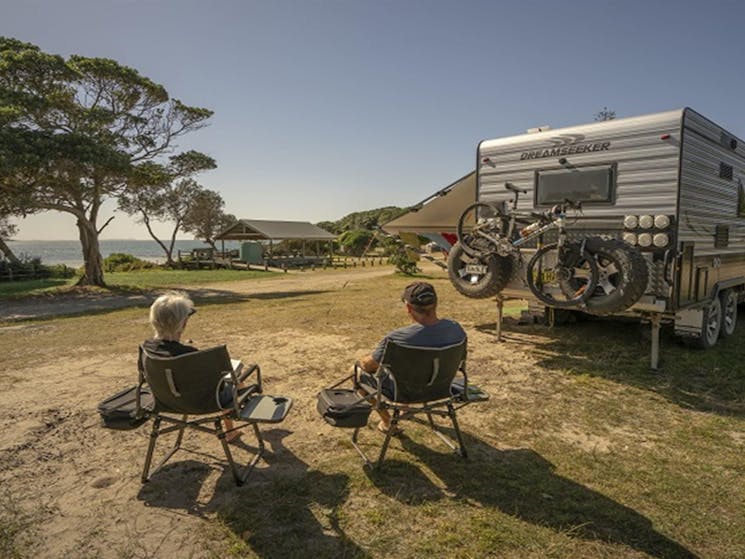 2 people sitting down beside their campervan looking out at the ocean at Point Plomer campground,