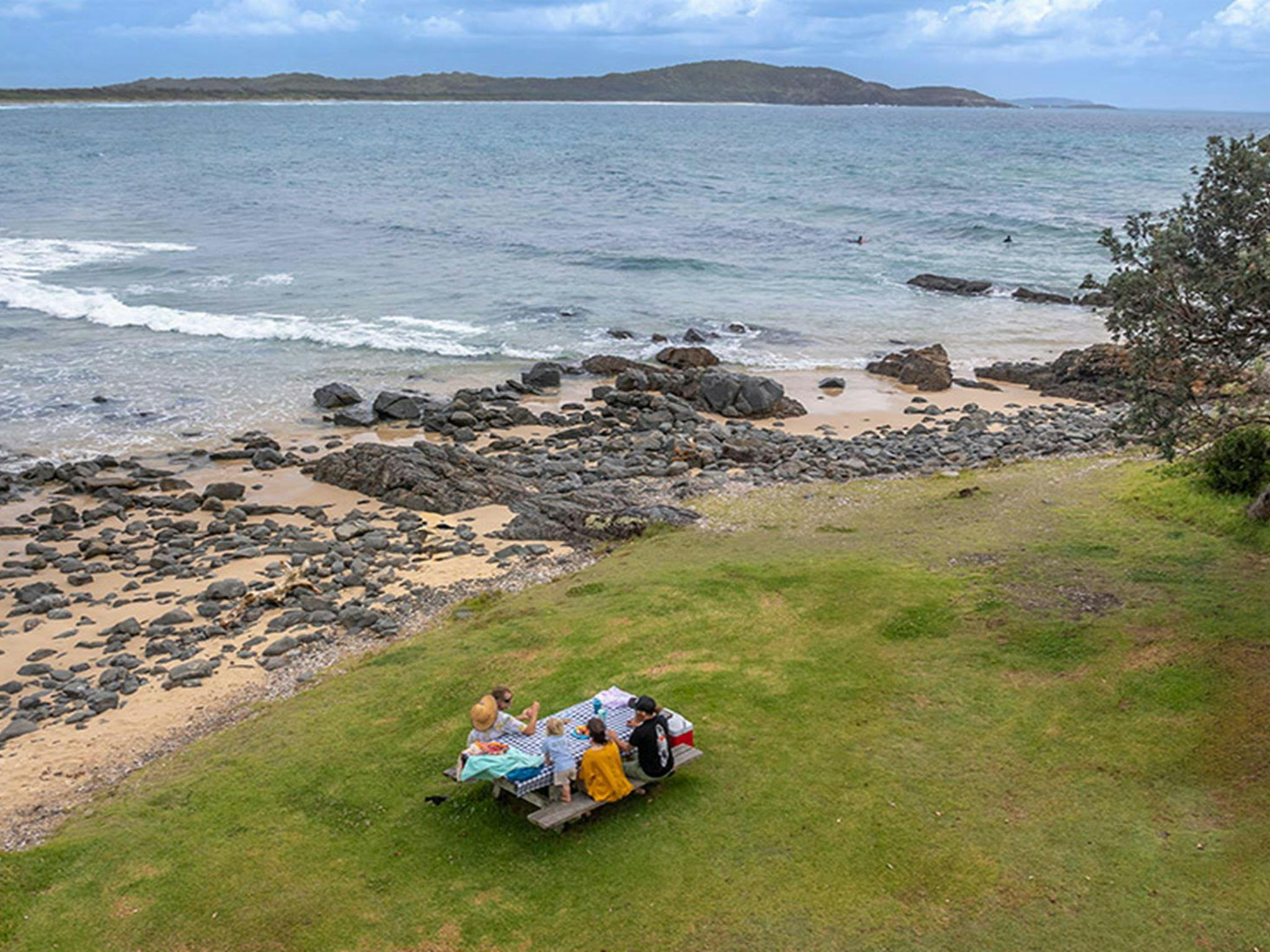 A family sitting at a picnic table by the beach at Point Plomer campground in Limeburners Creek