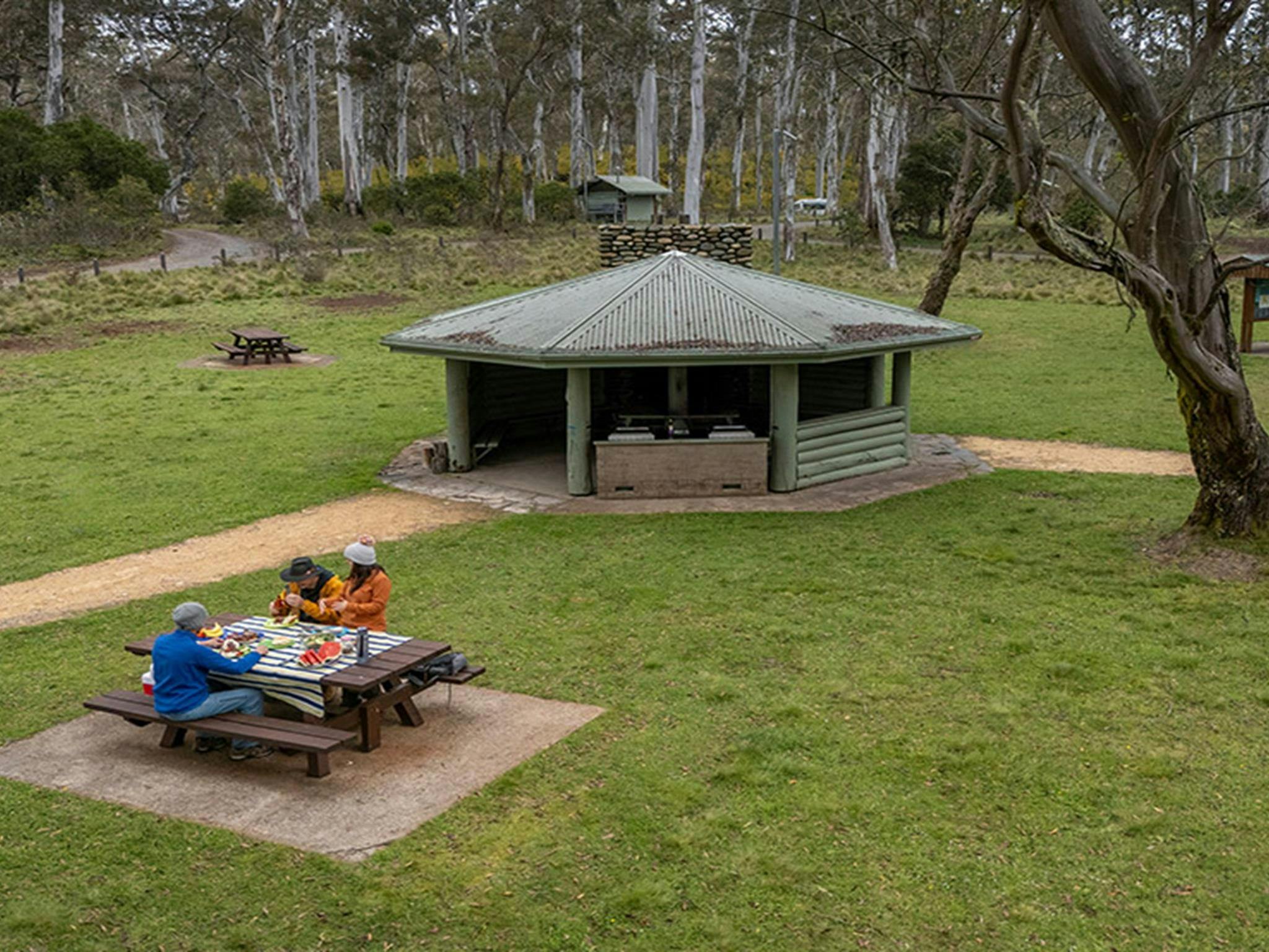 Zwei Personen essen an einem Picknicktisch in der Nähe von Grillmöglichkeiten unter einem überdachten Pavillon in Polblue.