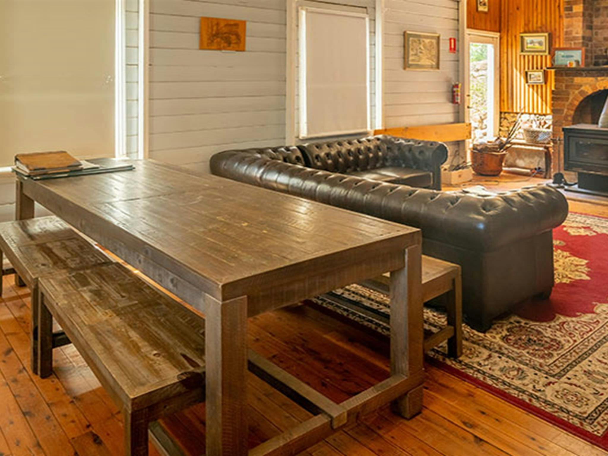 Ein langer Esstisch aus Holz, ein Sofa und ein Holzofen in der Post Office Lodge im Yerranderie Regional Park.