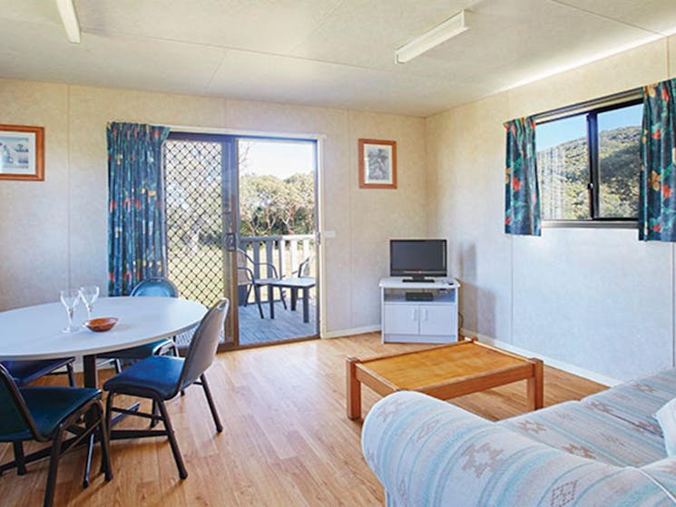 The dining and lounge room with dining table, couch and TV in Pretty Beach cabins, Murramarang