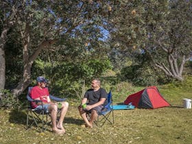 2 campers sitting down beside their tent talking at Racecourse campground. Photo: John Spencer/OEH