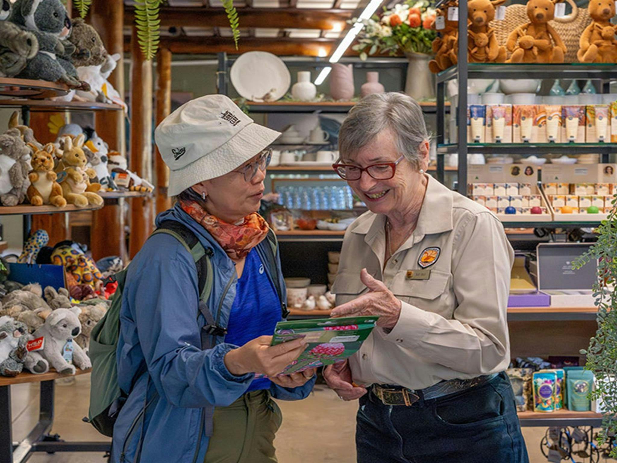 An NPWS staff member helping a visitor inside the Royal National Park Visitor Centre shop. Credit: