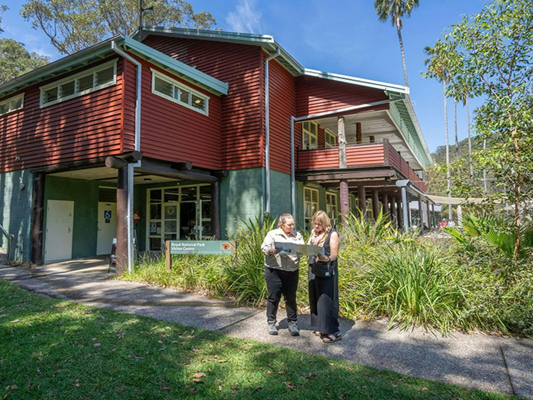 An NPWS staff member helping a visitor with a map outside the Royal National Park Visitor Centre.