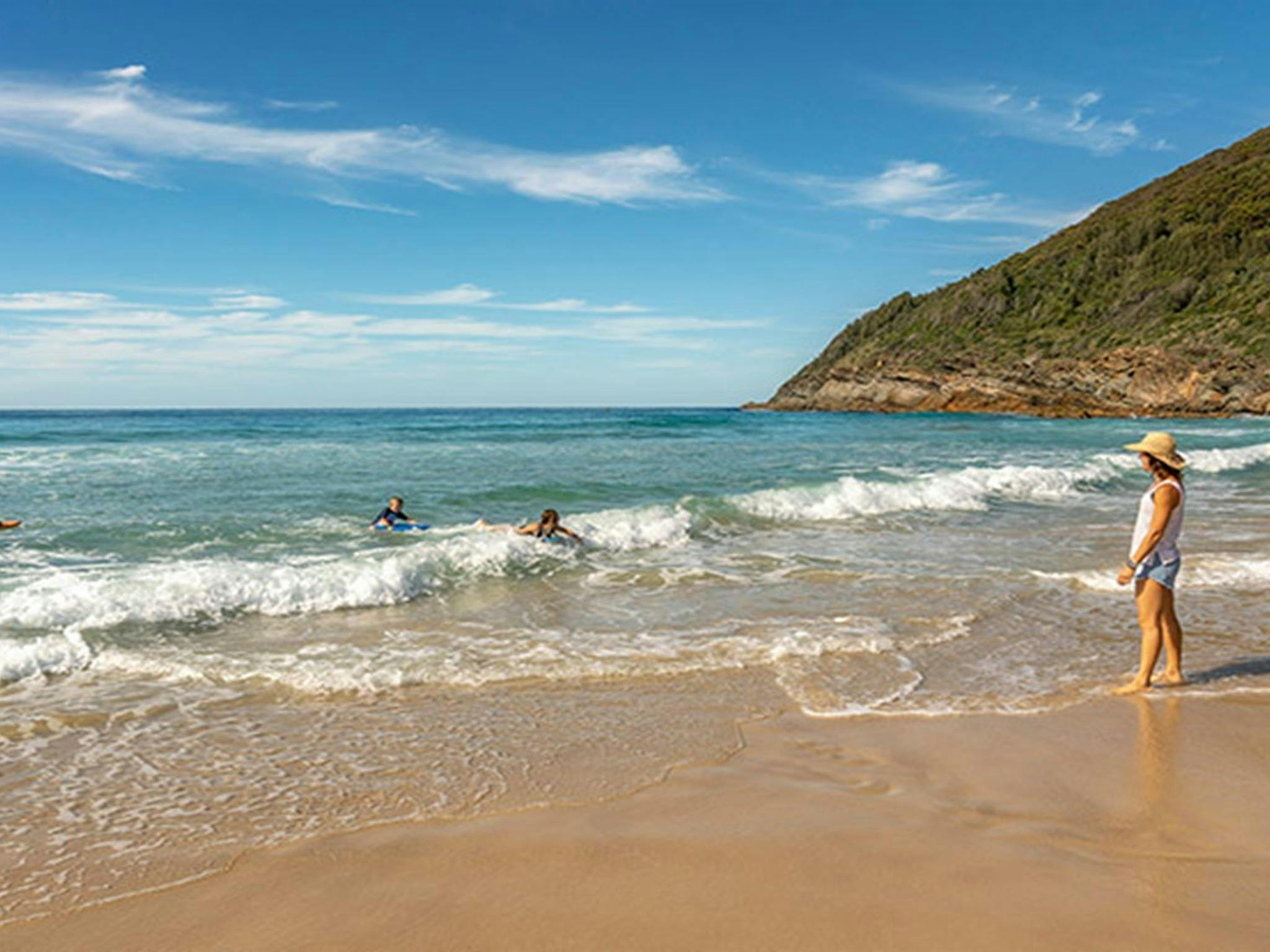 A mother watches her children play in the ocean, at Seven Mile Beach near The Ruins campground in