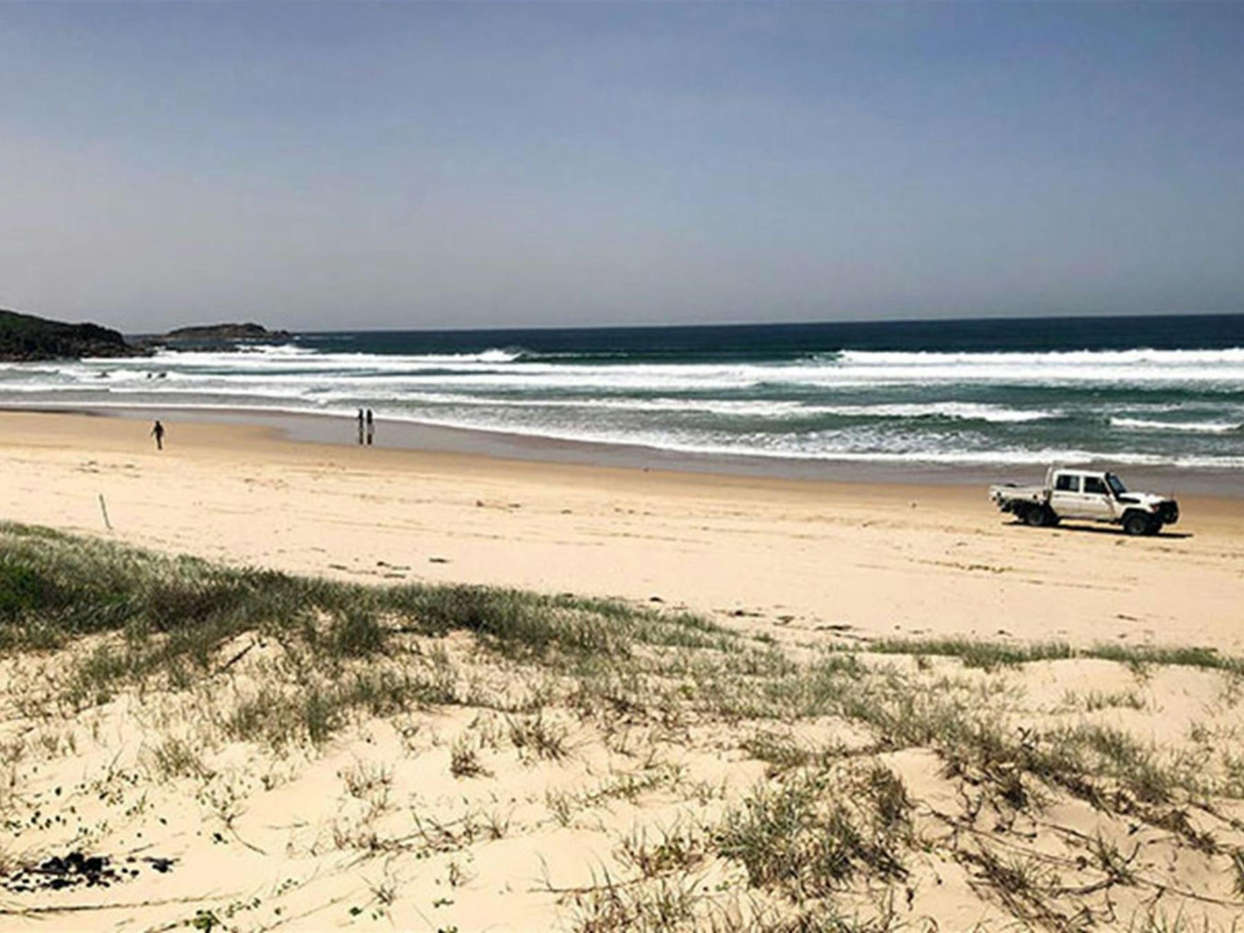 View across dunes to people and a vehicle on Samurai Beach and a distant headland. Photo: Jim Cutler