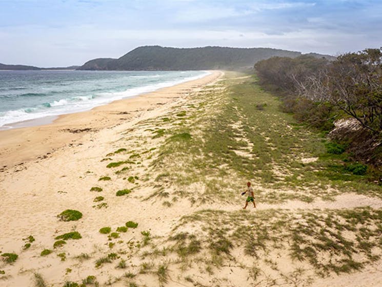 Aerial view of man crossing Seven Mile Beach with a distant headland in the background. Photo