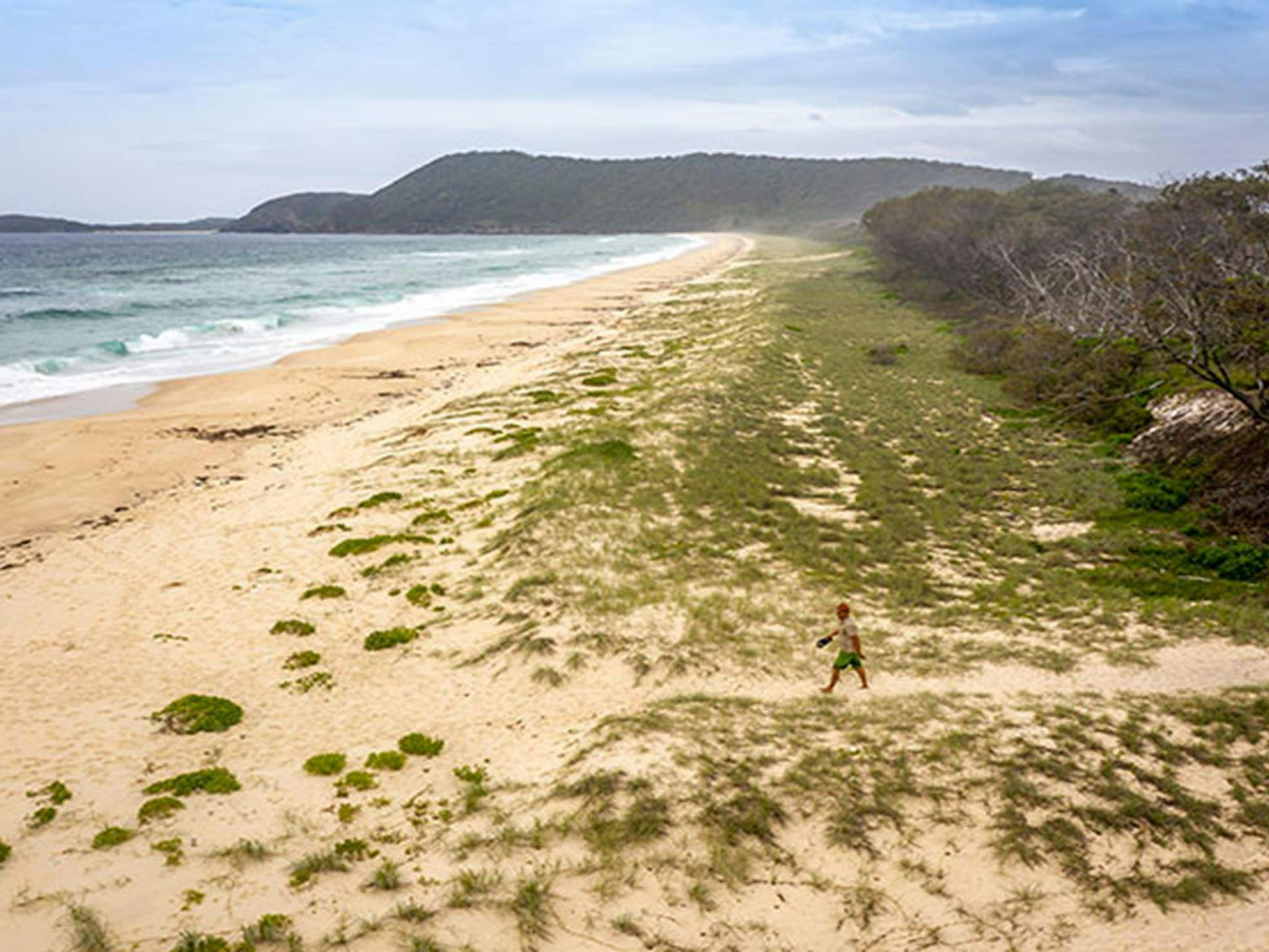 Aerial view of man crossing Seven Mile Beach with a distant headland in the background. Photo