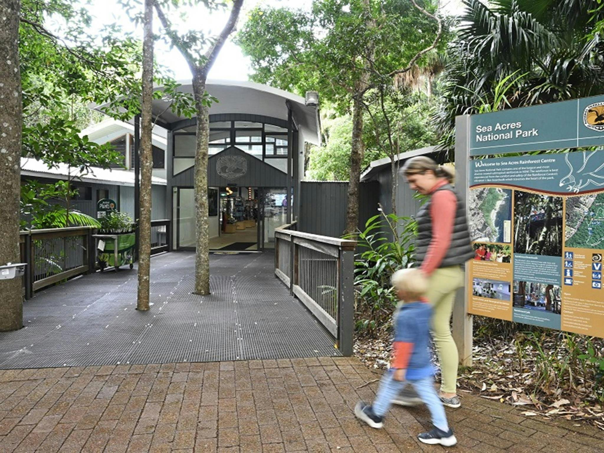 A woman and child walk towards the boardwalk entrance of Sea Acres Rainforest Centre, Sea Acres