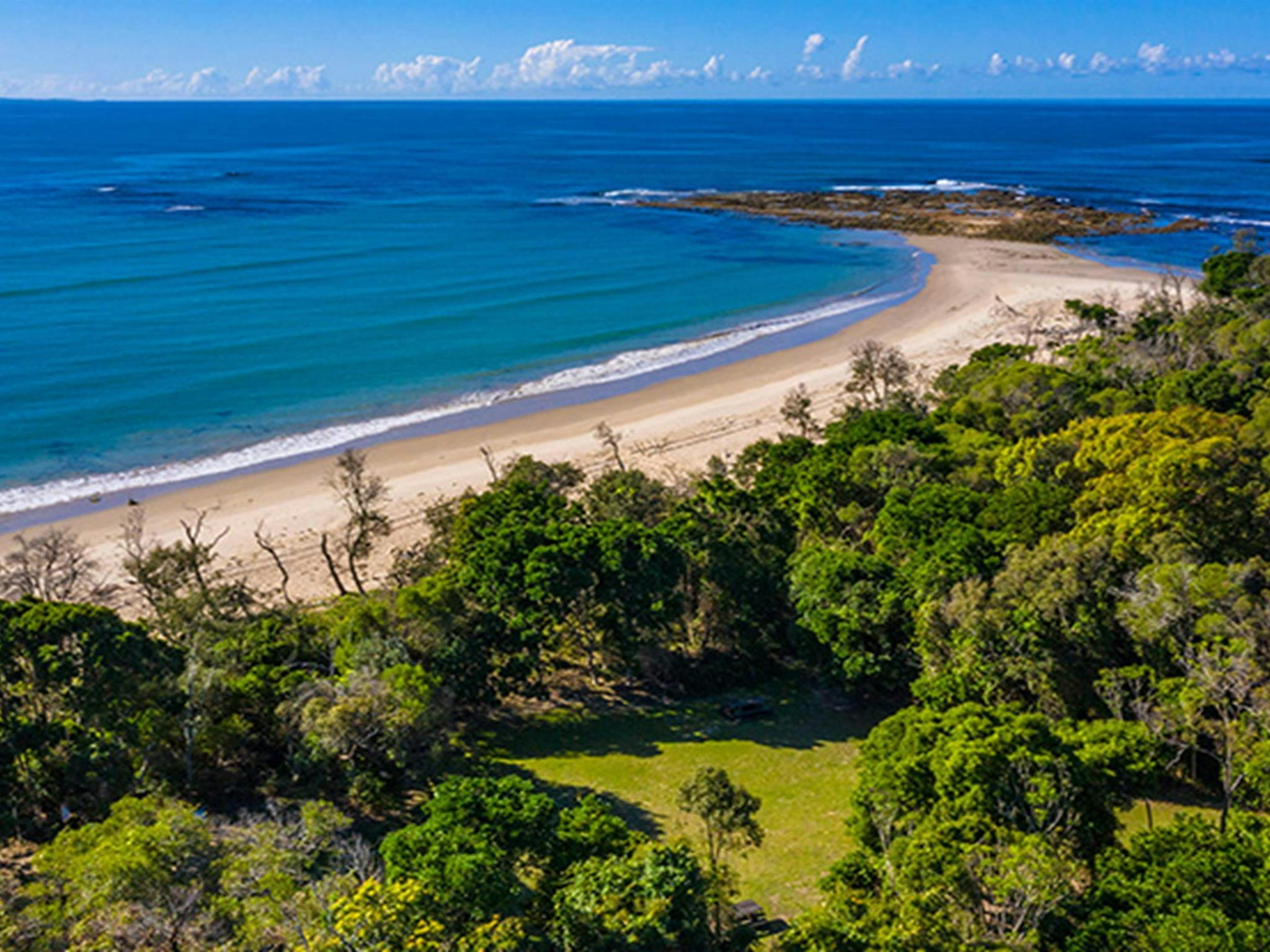 Aerial view of Shark Bay picnic area set in bushland, next to beach with rocky headland in the