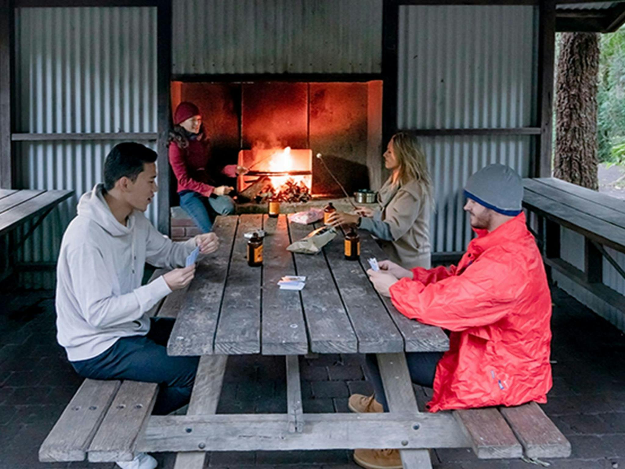 People sit at a table beside a fireplace under a picnic shelter at Sheepstation Creek campground,