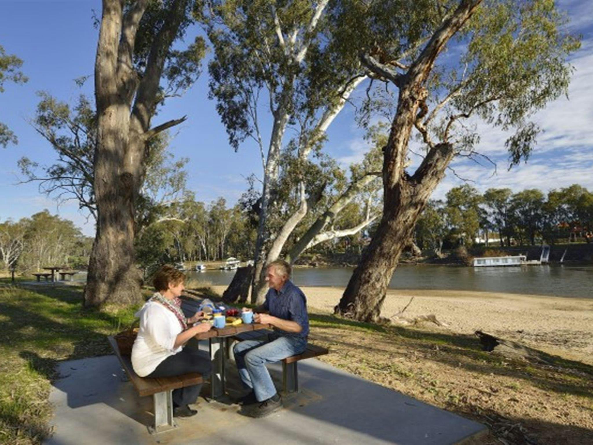 Two people at a picnic table at Ski Beach picnic area next to Murray River in Murray Valley Regional