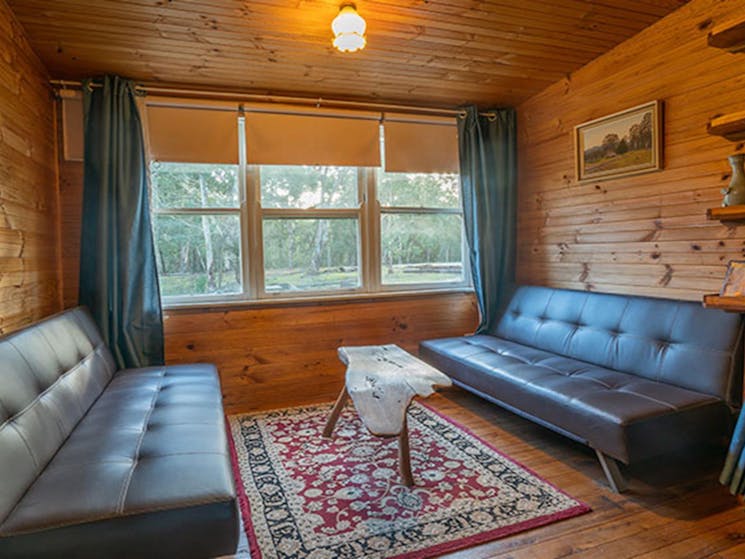 Two lounges and a wooden coffee table in Slippery Norris Cottage, Yerranderie Regional Park. Photo: