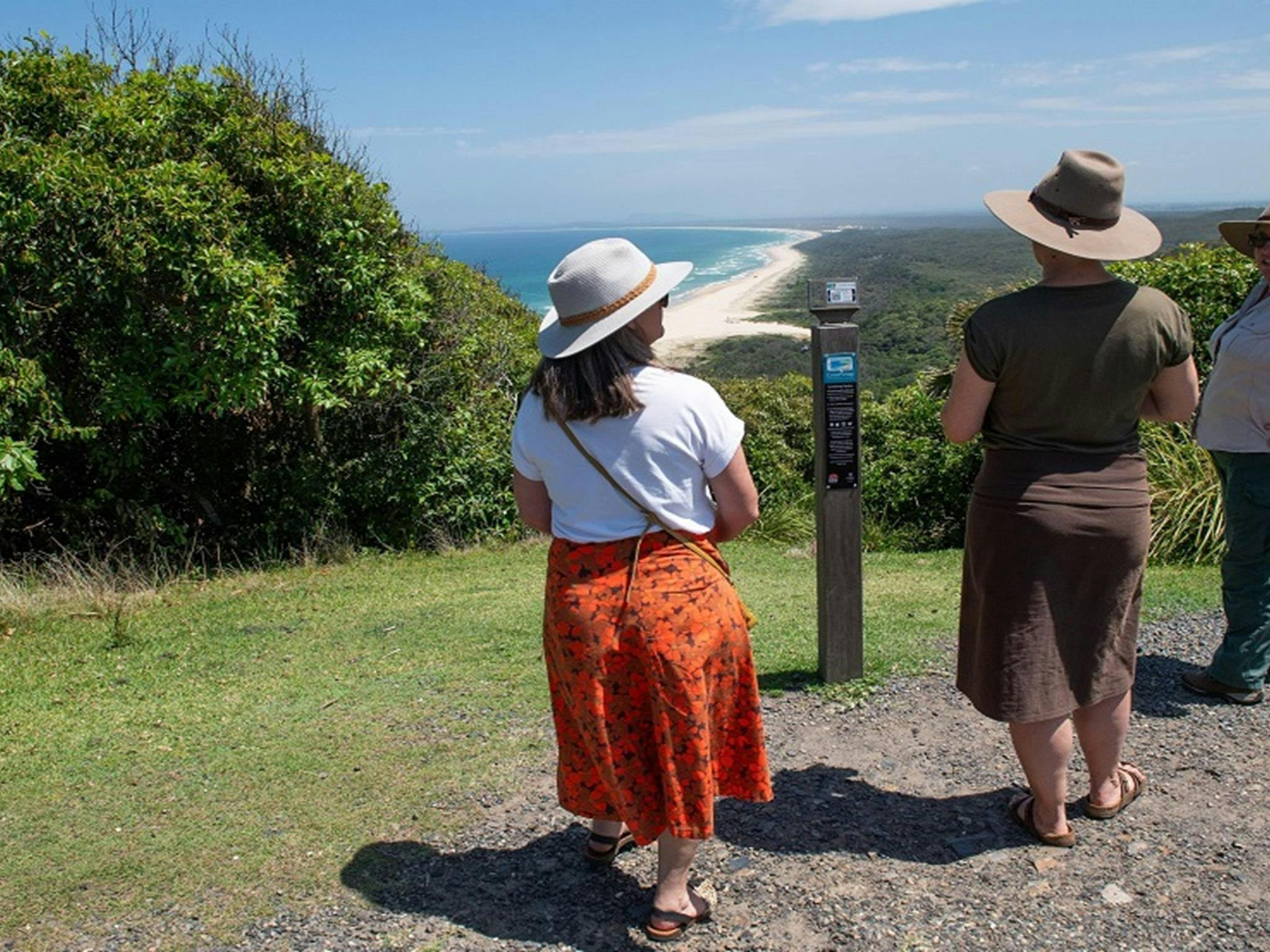 游客和国家公园及野生动物管理局的导游在灯塔草坪上聊天，欣赏着白沙滩和郁郁葱葱的树木。