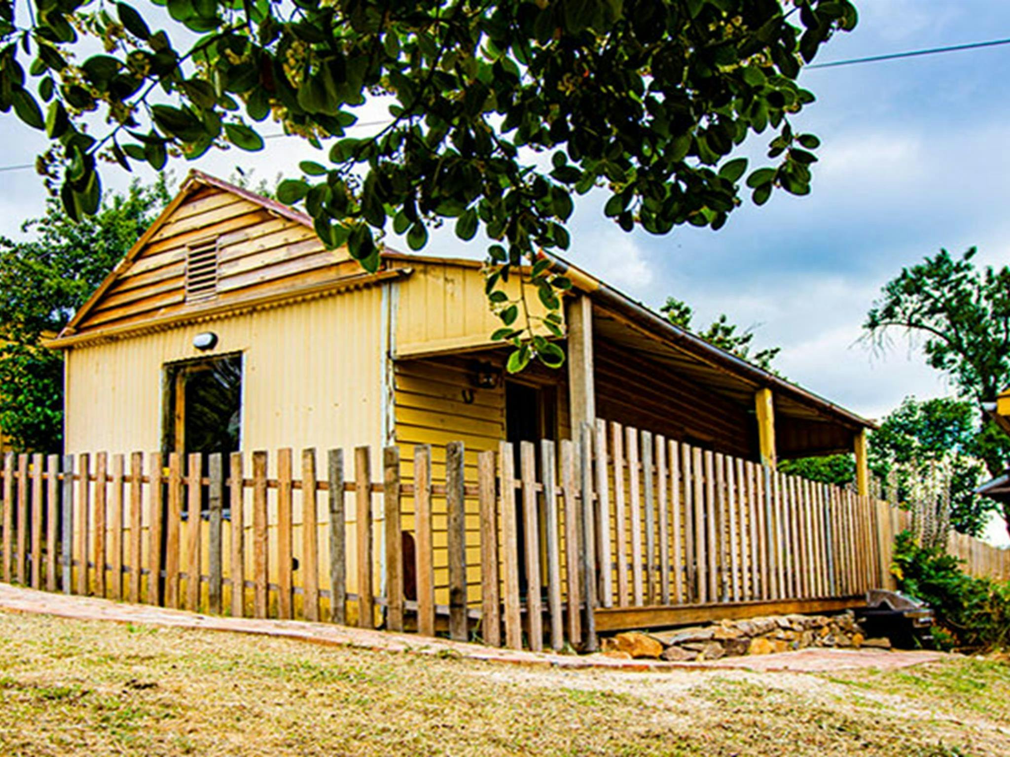 The exterior of Sydney Hotel Cottage surrounded by picket fence under trees in Hill End Historic