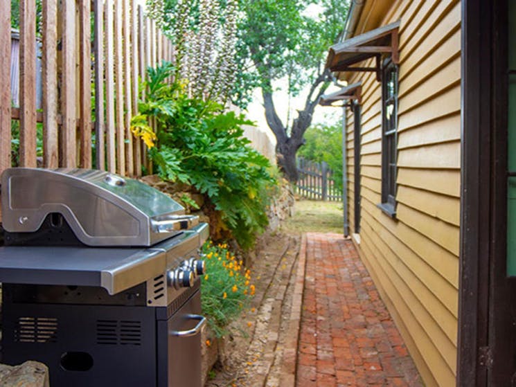 A pathway around the side of Sydney Hotel Cottage with barbecue and trees in the background. Photo: