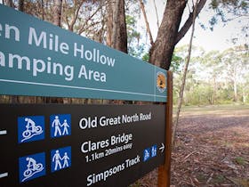 A visitor enters Ten Mile Hollow campground behind a sign for the campground in Dharug National Park