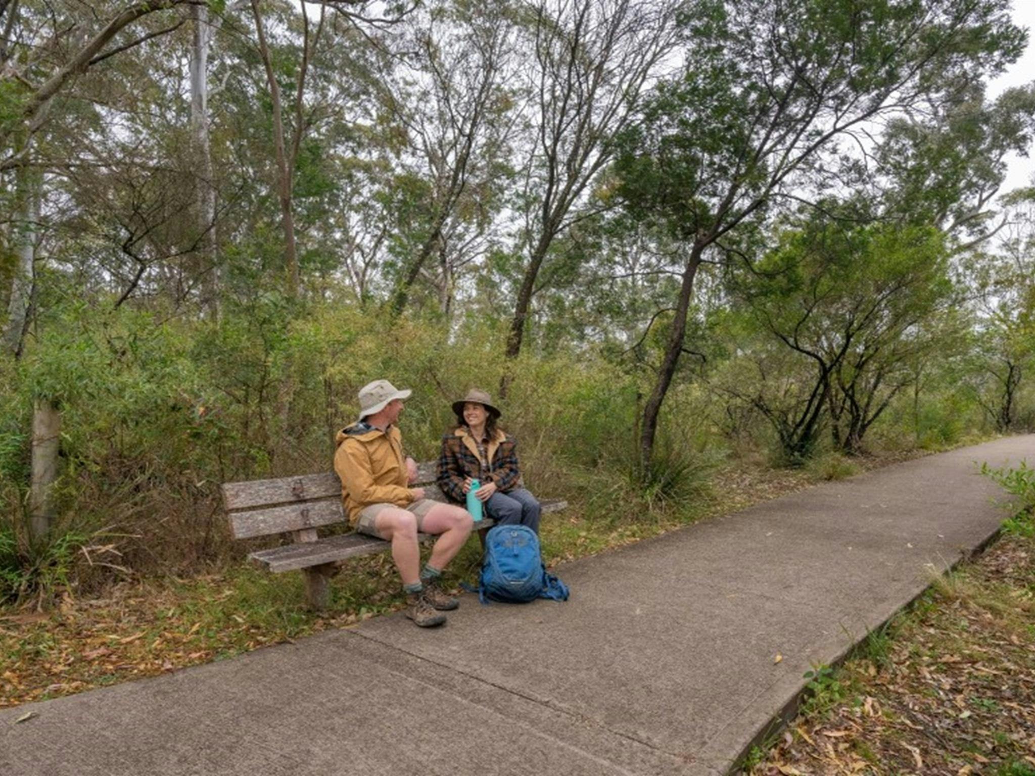 Two people sitting on a bench next to the path that leads to The Lookdown lookout in Bungonia