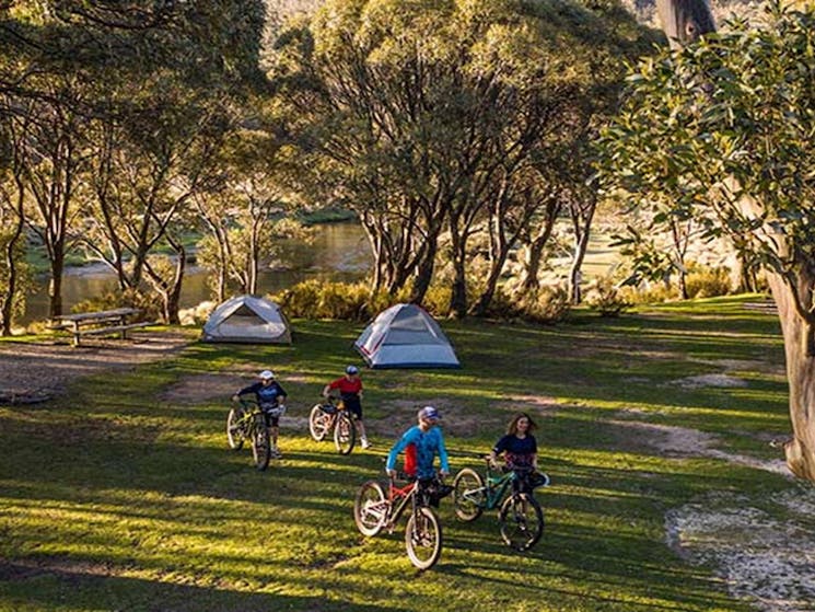 A family unloads bikes from a van and walks towards tents at Thredbo Diggings campground, Kosciuszko