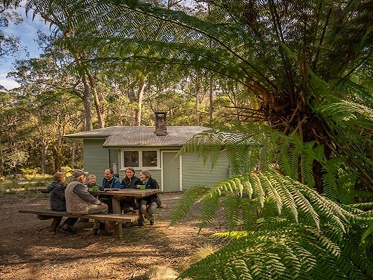 Family sitting around the picnic table outside Toms Cabin. Photo: John Spencer &copy; DPIE