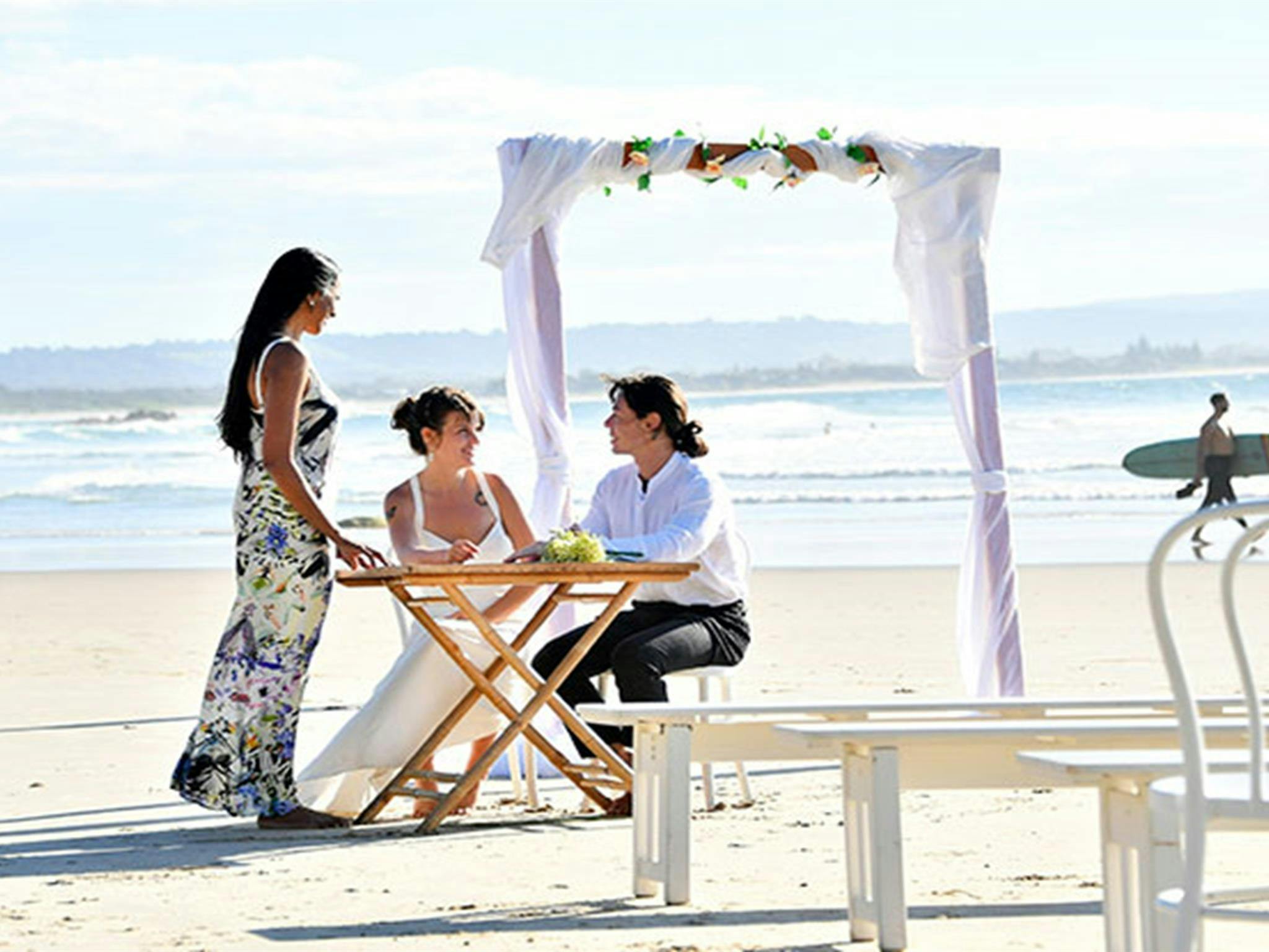 一对新人和他们的证婚人站在签字桌前，背景是婚礼拱门和大海。
