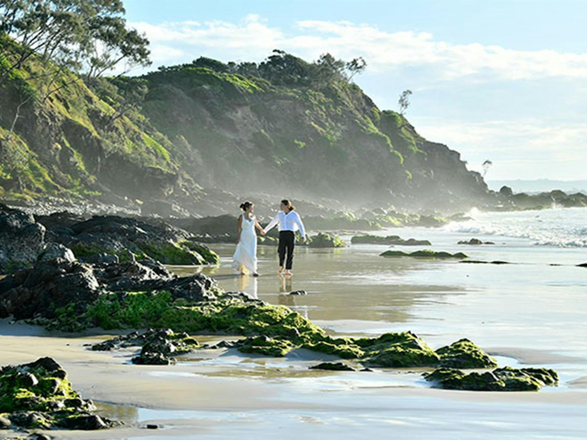 一对情侣漫步在拜伦角州立保护区沃特戈斯海滩的岩石和潮汐池旁。