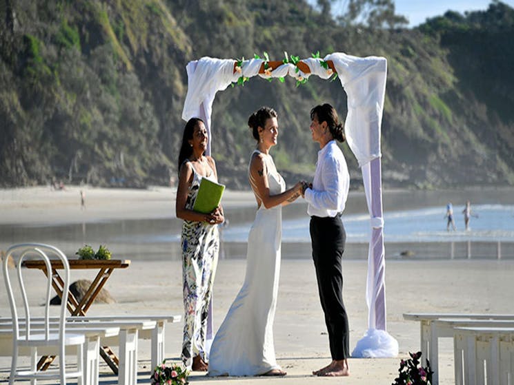 A couple saying their vows beneath a wedding arch on Wategos Beach in Cape Byron State Conservation