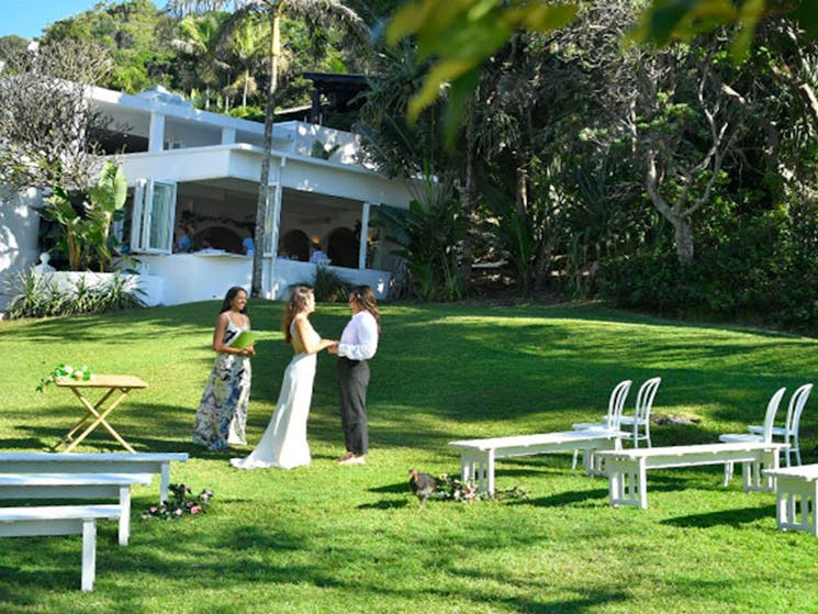 A couple and a celebrant saying their vows on Wategos lawn in Cape Byron State Conservation Area.
