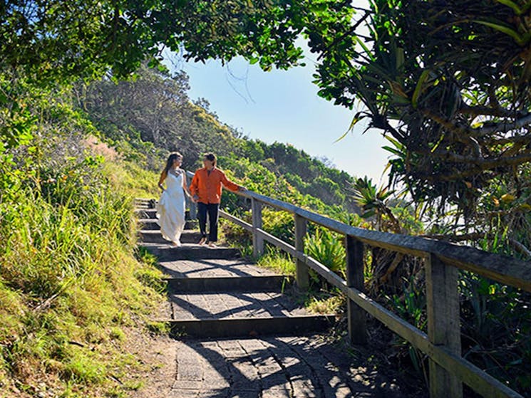 A couple walking down the stairs along a walkway overlooking Wategos Beach in Cape Byron State
