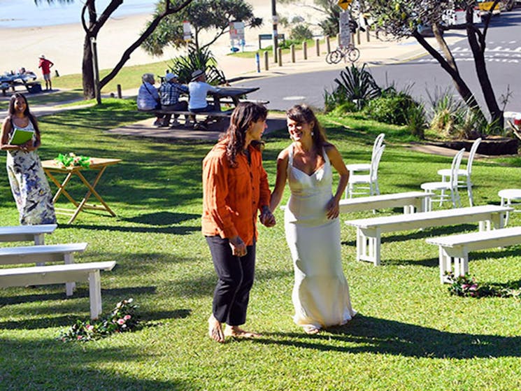 A joyful couple walking down the aisle after their wedding ceremony on Wategos lawn in Cape Byron