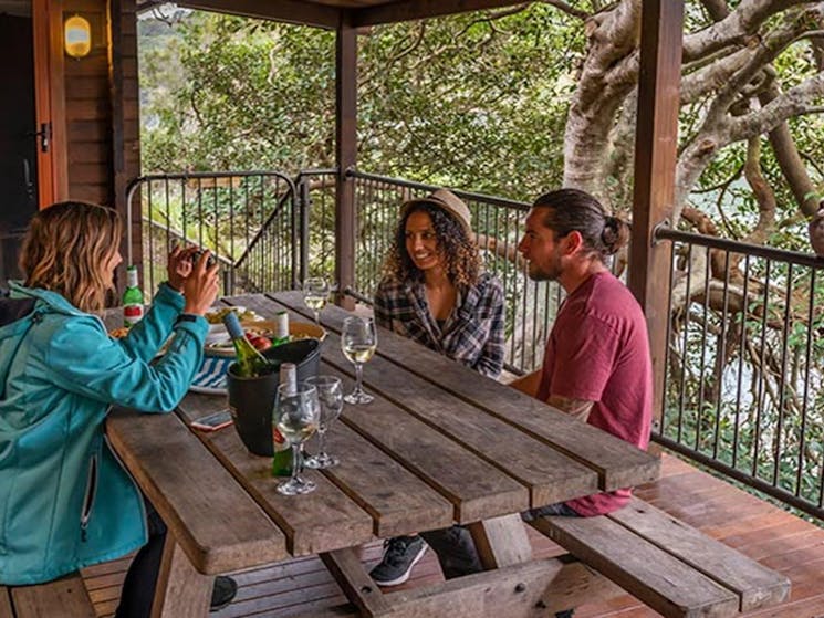 Four people drink wine at a table on the balcony of Weemalah Cottage, Royal National Park. Photo: