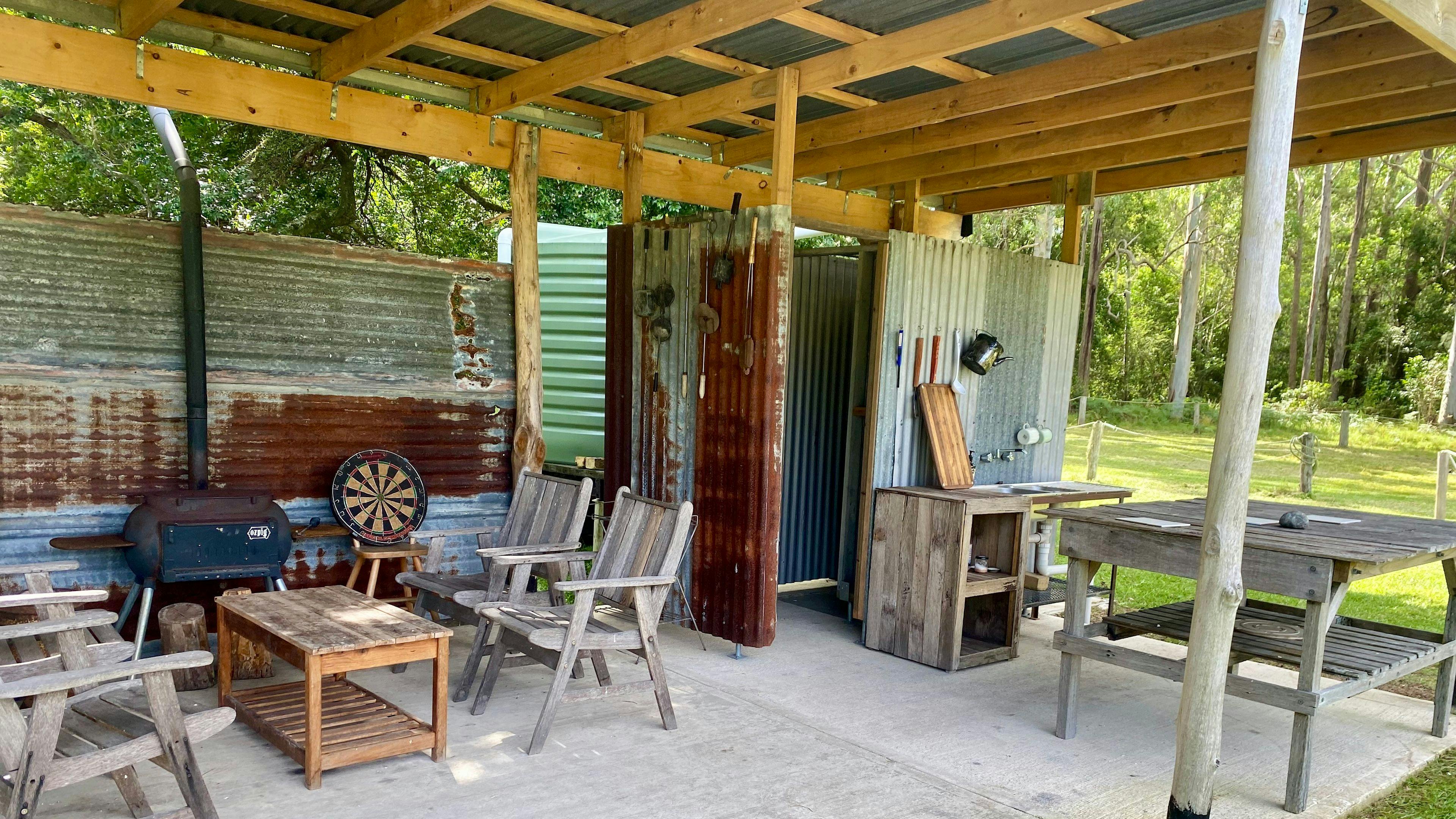 Inside shot of covered camping area including Oz Pig Big Pig, wooden camping furniture, sink, shower and rain water tank to the rear of the site