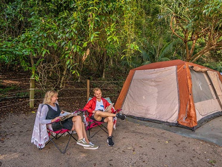 A couple relax, reading magazines beside their tent at Woody Head campground, Bundjalung National
